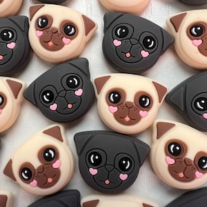 May include: A collection of 16 silicone pug charms in black and beige with pink hearts on their cheeks. The charms are in various poses and expressions.