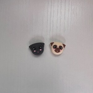 May include: Two pug dog phone charms, one black and one beige, with pink hearts for eyes.