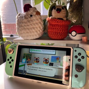 May include: A green and white Nintendo Switch console with a custom pug design on the joy-cons. The console is displaying the Animal Crossing: New Horizons game with the text "Good afternoon! We're so excited to have you here! ...have you here!" on the screen.