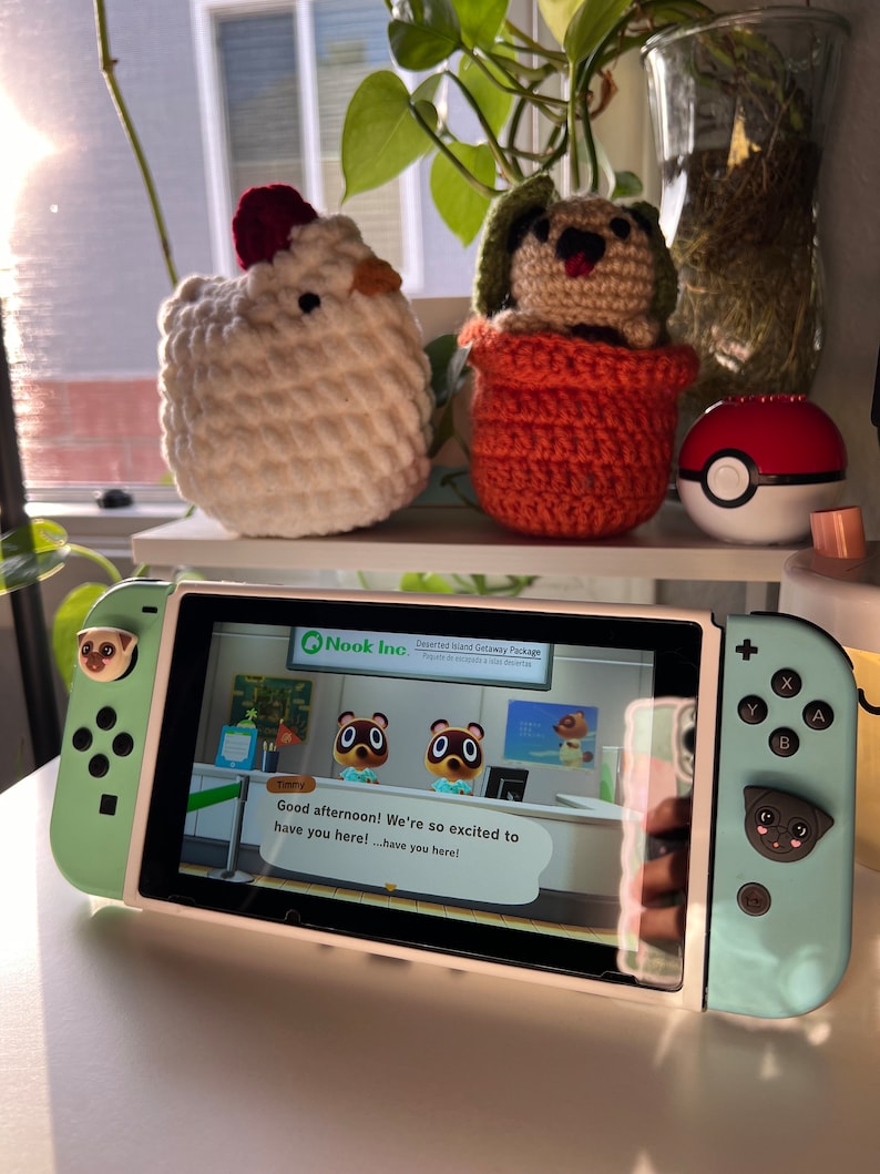 May include: A green and white Nintendo Switch console with a custom pug design on the joy-cons. The console is displaying the Animal Crossing: New Horizons game with the text "Good afternoon! We're so excited to have you here! ...have you here!" on the screen.