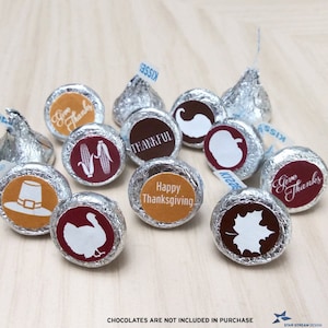 May include: Assortment of Thanksgiving-themed chocolate kiss stickers with various designs, including a pilgrim hat, a turkey, corn, a leaf, a pumpkin, and the words "Give Thanks" and "Happy Thanksgiving".