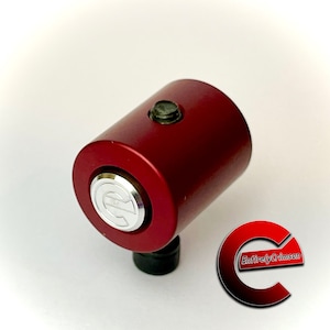 May include: A red metal cylinder with a silver button and a black base. The cylinder has a silver logo with the letter "C" on it. The text "Entirely Crimson" is visible in the background.