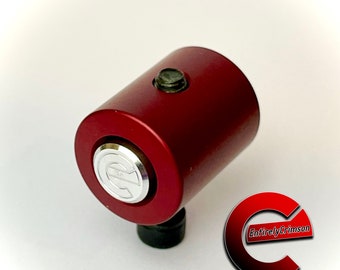 May include: A red metal cylinder with a silver button and a black base. The cylinder has a silver logo with the letter "C" on it. The text "Entirely Crimson" is visible in the background.