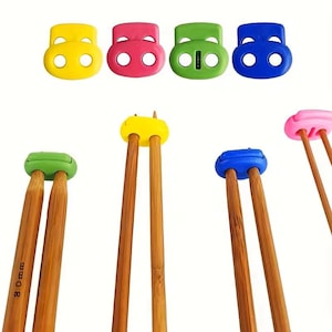 May include: A selection of brightly coloured knitting needle stoppers in yellow, pink, green, and blue. The stoppers are paired with wooden knitting needles. The needles are approximately 8 cm in length.
