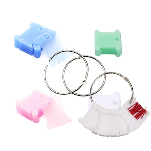 May include: A set of thread bobbins in blue, green, and pink, with three metal rings for organising them. There is also a white bobbin with a red thread.