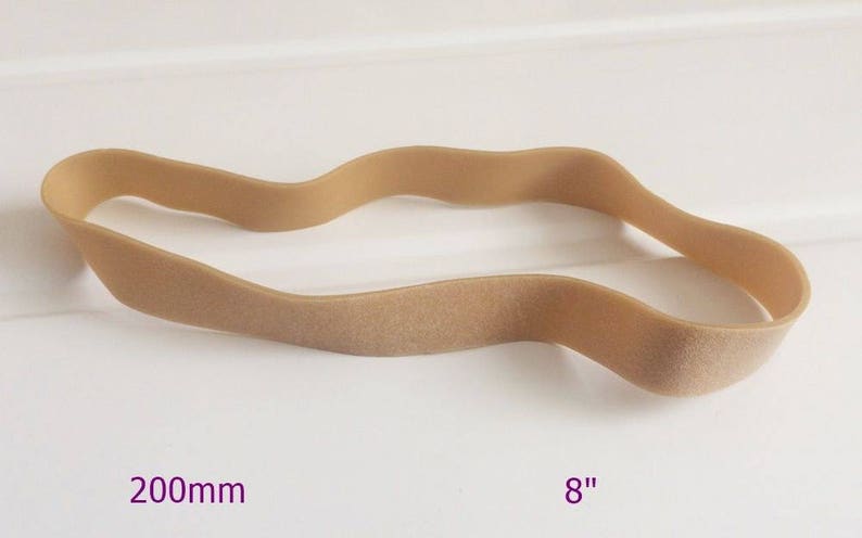 May include: A tan-coloured, wavy hair tie, approximately 20 cm in length, lies on a white surface. The hair accessory is made of a soft, flexible material. The image also includes the measurement in inches.