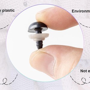 May include: Close-up of a black plastic safety eye with a white washer. The eye is being held by a hand. The text "High quality plastic", "Environment protection", "Safety", and "Not easy to bend" are visible around the eye.