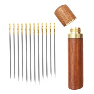May include: A set of 12 silver sewing needles with gold tips, stored in a wooden case with a brass top.