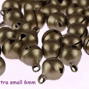 May include: A close-up of a pile of small, antique gold-coloured bells. The bells are about 6mm in diameter and have a small loop at the top for hanging.  Extra small 6mm.