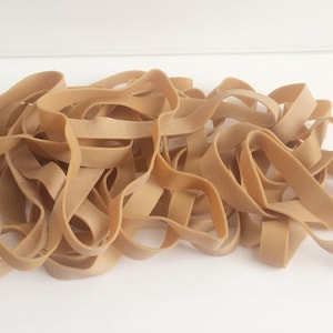 May include: A collection of tan-coloured rubber bands, with a slightly wavy texture, are arranged on a white surface. The bands vary in length and width. The text "20 x Bands" is visible in the lower right corner.