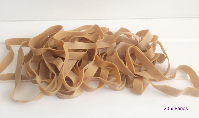 May include: A collection of tan-coloured rubber bands, with a slightly wavy texture, are arranged on a white surface. The bands vary in length and width. The text "20 x Bands" is visible in the lower right corner.