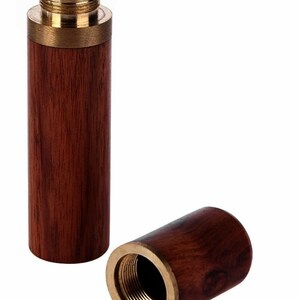 May include: A wooden and brass needle threader. The threader is made of dark wood with a brass top and bottom. The threader is open and the inside is visible.