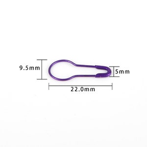 May include: A purple safety pin measuring 22.0 mm in length, 9.5 mm in height, and 5 mm in width.