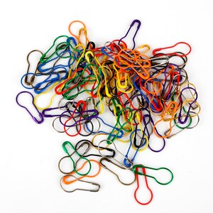 May include: A large pile of colorful safety pins in various shades of red, orange, yellow, green, blue, and purple.