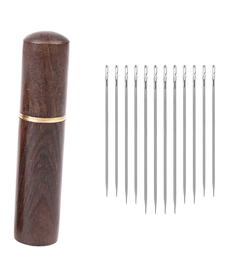 May include: A set of 10 silver sewing needles in a wooden case with a gold band. The case is made of dark brown wood with a wood grain pattern.