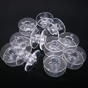 May include: A pile of clear plastic bobbins for a sewing machine.