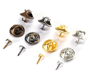 May include: A collection of metal pin backs and clasps in various finishes, including gold, silver, and bronze. The pin backs have a butterfly clutch design, and the clasps have a round shape. The image is on a white background.