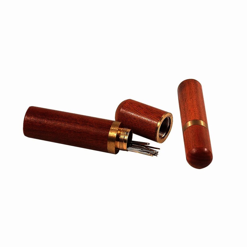 May include: A wooden needle case with a brass top and a set of needles inside. The case is open and the needles are visible. The case is made of dark wood with a reddish hue.