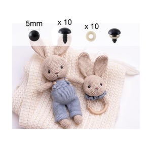 May include: Two crocheted bunny toys, one wearing blue overalls and the other with a wooden ring, on a white knitted blanket. The image also shows 5mm black safety eyes, 10mm black safety eyes, and 10mm white safety eyes.