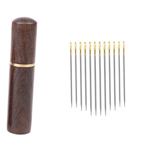 May include: A set of 12 silver sewing needles with gold tips, stored in a wooden case with a gold trim.