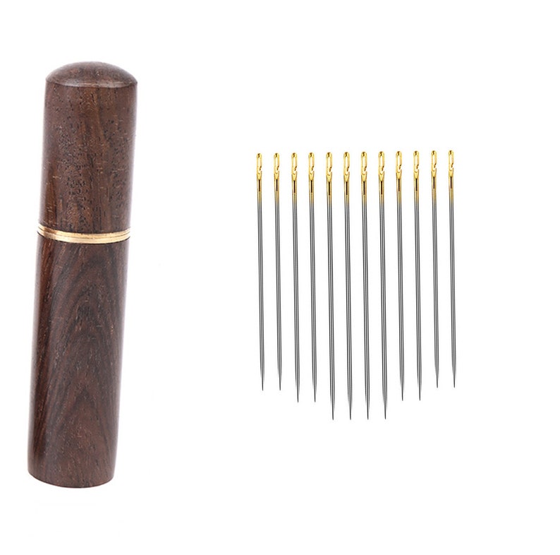 May include: A set of 12 silver sewing needles with gold tips, stored in a wooden case with a gold trim.