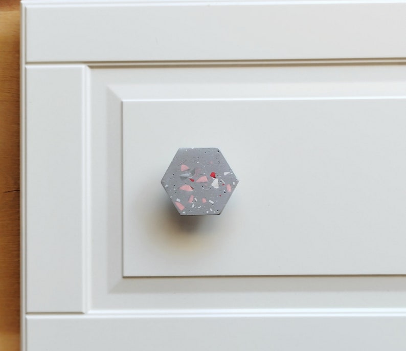 K&ouml;nnte beinhalten: Ein sechseckiger Schrankknopf aus grauem Beton mit rosa und roten Flecken.