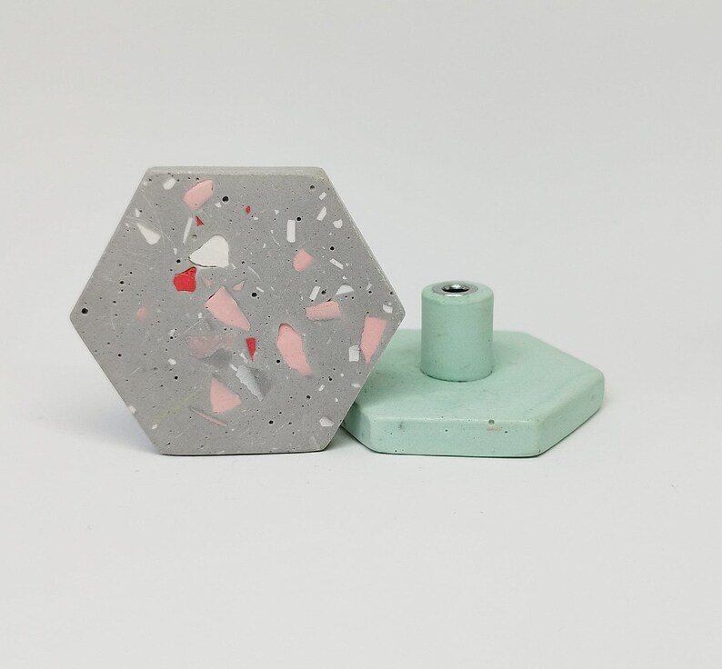 K&ouml;nnte beinhalten: Zwei sechseckige Schrankkn&ouml;pfe. Einer ist grau mit rosa und wei&szlig;en Flecken, der andere ist hellgr&uuml;n. Beide haben eine silberne Schraube in der Mitte.