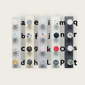 K&ouml;nnte beinhalten: Ein Satz von 26 bunten Kn&ouml;pfen mit verschiedenen Mustern und Farben, darunter Schwarz, Wei&szlig;, Rot, Rosa, Gelb, Blau und Gr&uuml;n. Die Kn&ouml;pfe sind in alphabetischer Reihenfolge von A bis Z auf einem wei&szlig;en Hintergrund angeordnet.