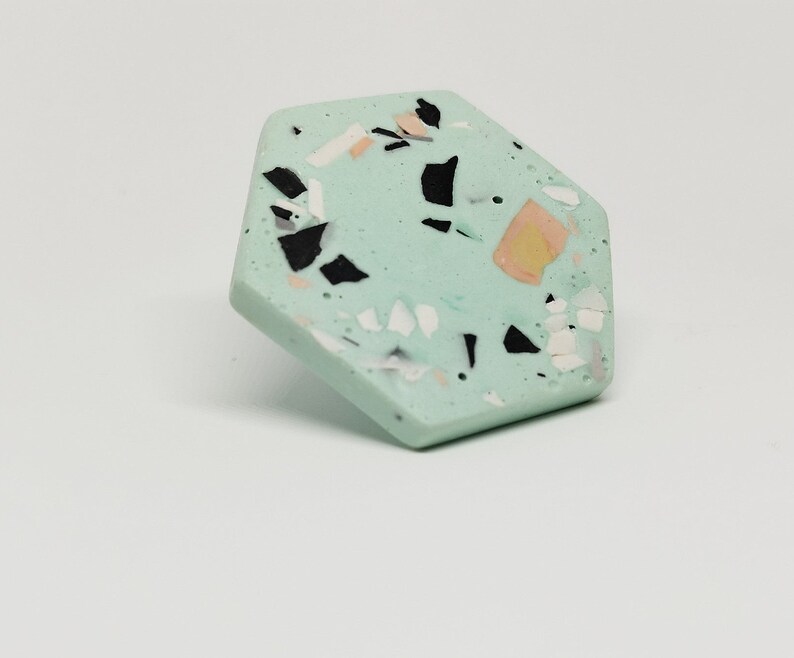 K&ouml;nnte beinhalten: Ein sechseckiger Untersetzer mit einer hellgr&uuml;nen Basis und einem gesprenkelten Muster aus Schwarz, Wei&szlig; und Pfirsich.