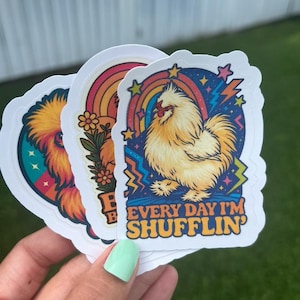 Könnte beinhalten: Drei bunte Aufkleber mit Hühnern. Ein Aufkleber hat einen Regenbogen und den Text "Every Day I'm Shufflin'". Die anderen Aufkleber zeigen ein Huhn mit Regenbogen und Blumen.