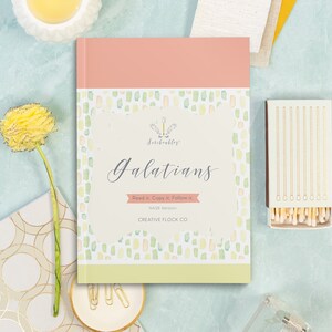 May include: A hardcover book titled "Galatians" with a pink and green cover, and the text "Read it. Copy it. Follow it." A box of matches and a yellow flower are also visible.