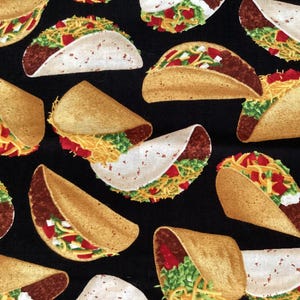 May include: A black fabric featuring a repeating pattern of tacos. Each taco is depicted with a golden-brown shell, dark brown seasoned meat, shredded green lettuce, bright yellow shredded cheese, and diced red tomatoes.