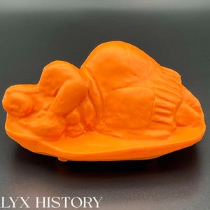 Könnte beinhalten: Orangefarbene Plastikskulptur einer liegenden Person. Die Skulptur ist detailliert und hat eine glatte Oberfläche.