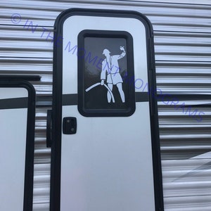 May include: A white door with a black frame and a black handle. A small window with a black frame is in the center of the door. A silhouette of a person holding a hose is visible in the window.