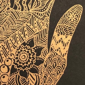 K&ouml;nnte beinhalten: Ein schwarzer Hintergrund mit einem goldenen handgezeichneten Design. Das Design ist kompliziert und detailliert und zeigt eine Vielzahl von Mustern und Formen. Die Hand ist stilisiert gezeichnet, mit gespreizten Fingern.
