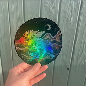Könnte beinhalten: Ein runder, holografischer Aufkleber mit einem Elch-Design in Regenbogenfarben. Der Elch ist mit aufwendigen Mustern verziert, vor einem sternenklaren Nachthimmel mit einem Halbmond. Der Aufkleber hat den Text "Seventh Petal Design".
