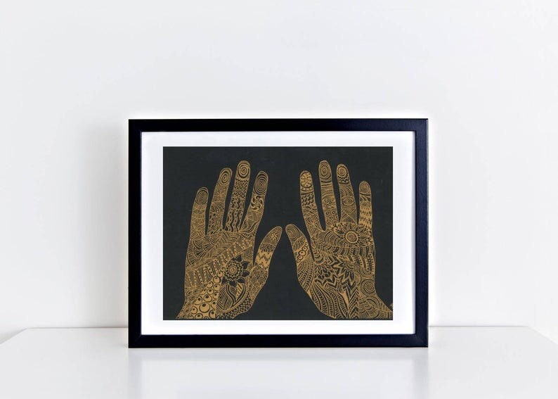 K&ouml;nnte beinhalten: Ein gerahmter Druck von zwei H&auml;nden mit aufwendigen goldenen Henna-Designs auf schwarzem Hintergrund.