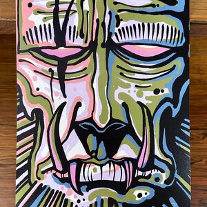 May include: Abstract painting of a stylized face with closed eyes and sharp teeth. The artwork features a color palette of black, green, pink, blue, and white. The painting is on a rectangular canvas.