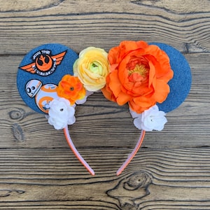 May include: Denim-style mouse ears with orange and yellow flowers. One ear features a patch with the text "Join the Resistance" and a BB-8 graphic. The headband is white and orange.