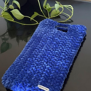 May include: A vibrant blue, hand-crocheted tote bag with a plush, textured surface. The bag features two handles and a small, rectangular tag with the text "ECBCREATIONS". The bag is made of a soft, thick yarn.