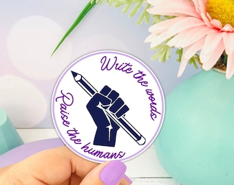 May include: A white round sticker with a purple fist holding a pencil. The text on the sticker reads "Write the words, Raise the humans".