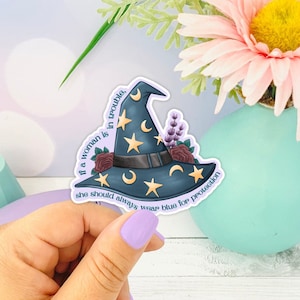 May include: A blue witch hat with stars and moons, surrounded by flowers. The text reads "If a woman is in trouble, she should always wear blue for protection."