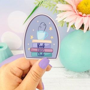 May include: A purple and blue sticker with a stack of books, a cup of coffee with steam, and stars. The text on the sticker reads "Book Lovers Club".
