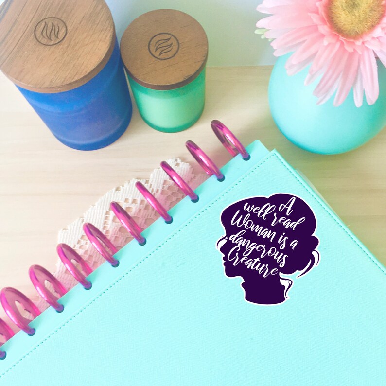 May include: A teal blue planner with a pink coil binding. A purple silhouette of a woman's head with the text "A well read woman is a dangerous creature" in white.