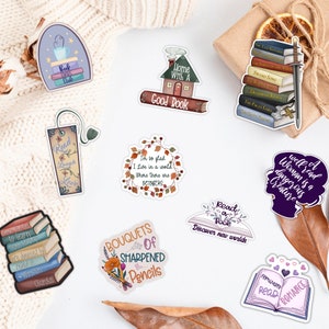 May include: A set of 10 book-themed stickers featuring various designs, including a house with the text "Home With A Good Book", a stack of books with a sword, a wreath with the text "I'm so glad I live in a world where there are Octobers", a book with the text "Read a Book Discover New Worlds", and a bouquet of sharpened pencils.