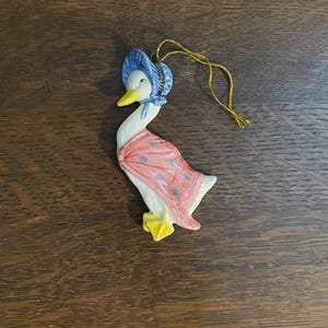 Puede incluir: Adorno de cerámica con forma de ganso, con un gorro azul y un chal rosa con lunares azules. El ganso tiene pico y patas amarillas, y una cuerda dorada para colgar. Ideal para decoración navideña.