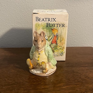 May include: A Beatrix Potter ceramic figurine of a rabbit in a green coat and yellow waistcoat, seated with legs outstretched. A box with the words "Beatrix Potter" and an illustration of a fox and rabbit is behind.