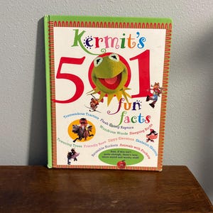 May include: A children's book titled "Kermit's 501 Fun Facts" featuring Kermit the Frog on the cover. The book has a green border and a red and white patterned border. The cover includes various cartoon illustrations and text.