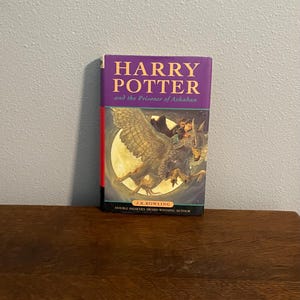 May include: A purple and red hardcover book with the title "Harry Potter and the Prisoner of Azkaban" by J.K. Rowling. The cover features an illustration of Harry Potter flying on a Hippogriff.
