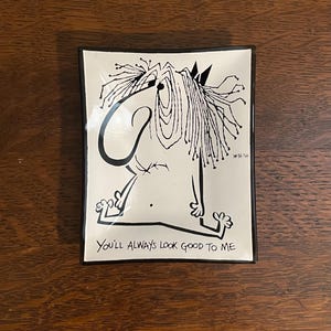 May include: A white ceramic tray with a black and white illustration of a person with long hair. The tray has a black border and the text "You'll always look good to me".